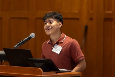 A college-age speaker smiles while talking at a lectern.