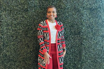 A woman, smiling, stands in front of a green wall.